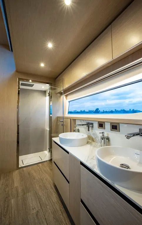 Modern bathroom featuring two white sinks, a glass shower, marble surfaces, and a window with scenic views.